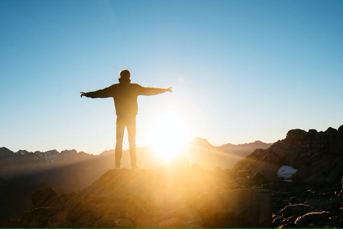 Person stood on rock with arms outstretched in front of sunrise